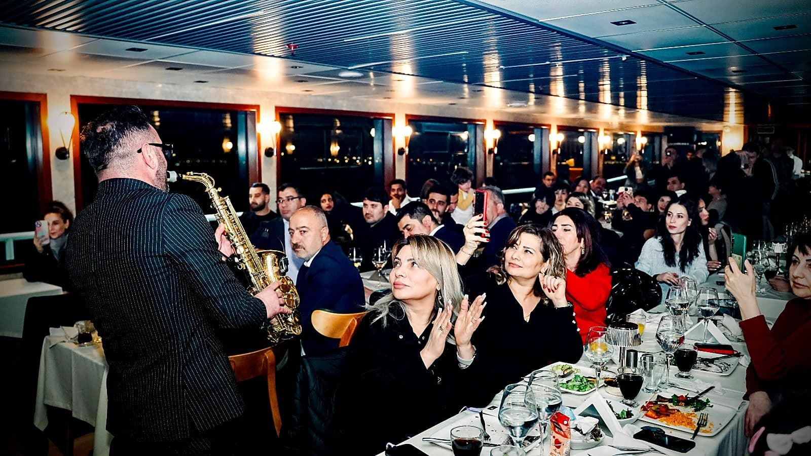 Guests at their dinner tables watching a saxophonist on board