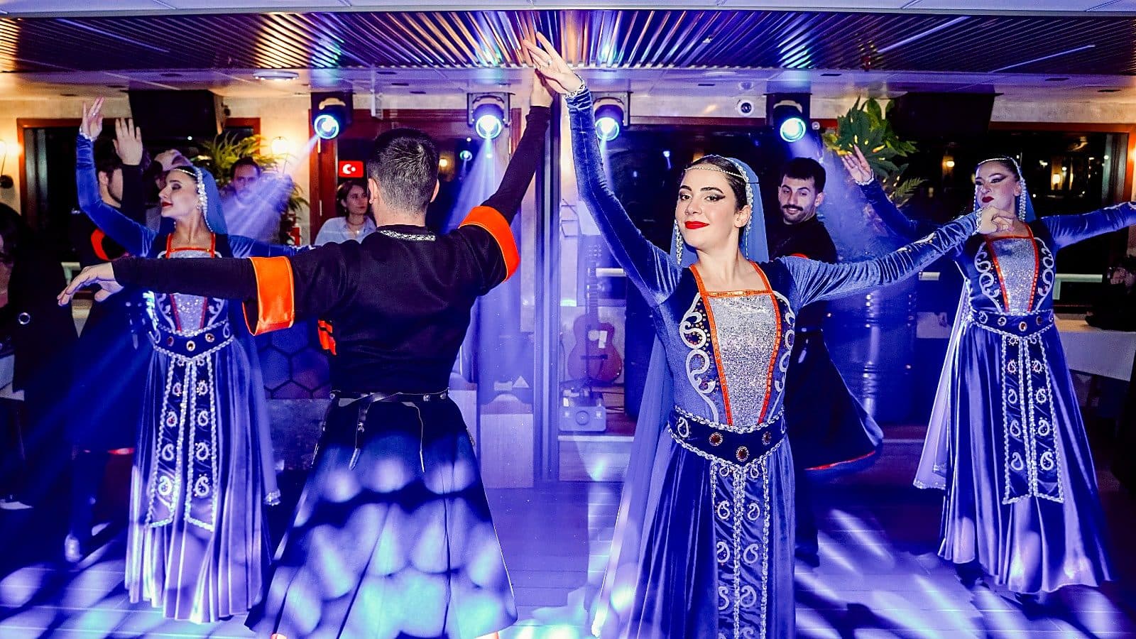 Folk dancers in blue costumes performing on board the night cruise